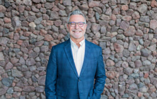 Paul Thyssen, Gallery Systems General Manager. Wearing a blue suit with a white shirt in front of a stone wall.