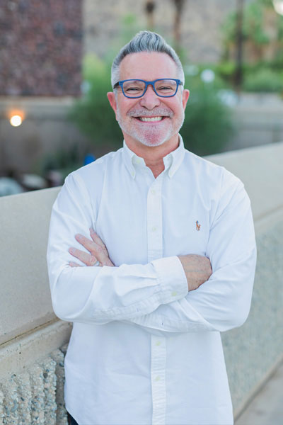 Paul Thyssen Gallery Systems Bio Photo. Paul is wearing a white long-sleeve shirt and glasses. He is smiling with his arms crossed.